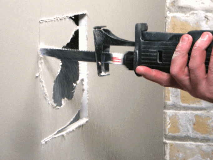 drywall-cutout-removal.png Contractor using a drywall saw to remove damaged drywall before installing a new patch.